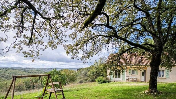 A rustic house with a garden, a swing set, and a view of the countryside.