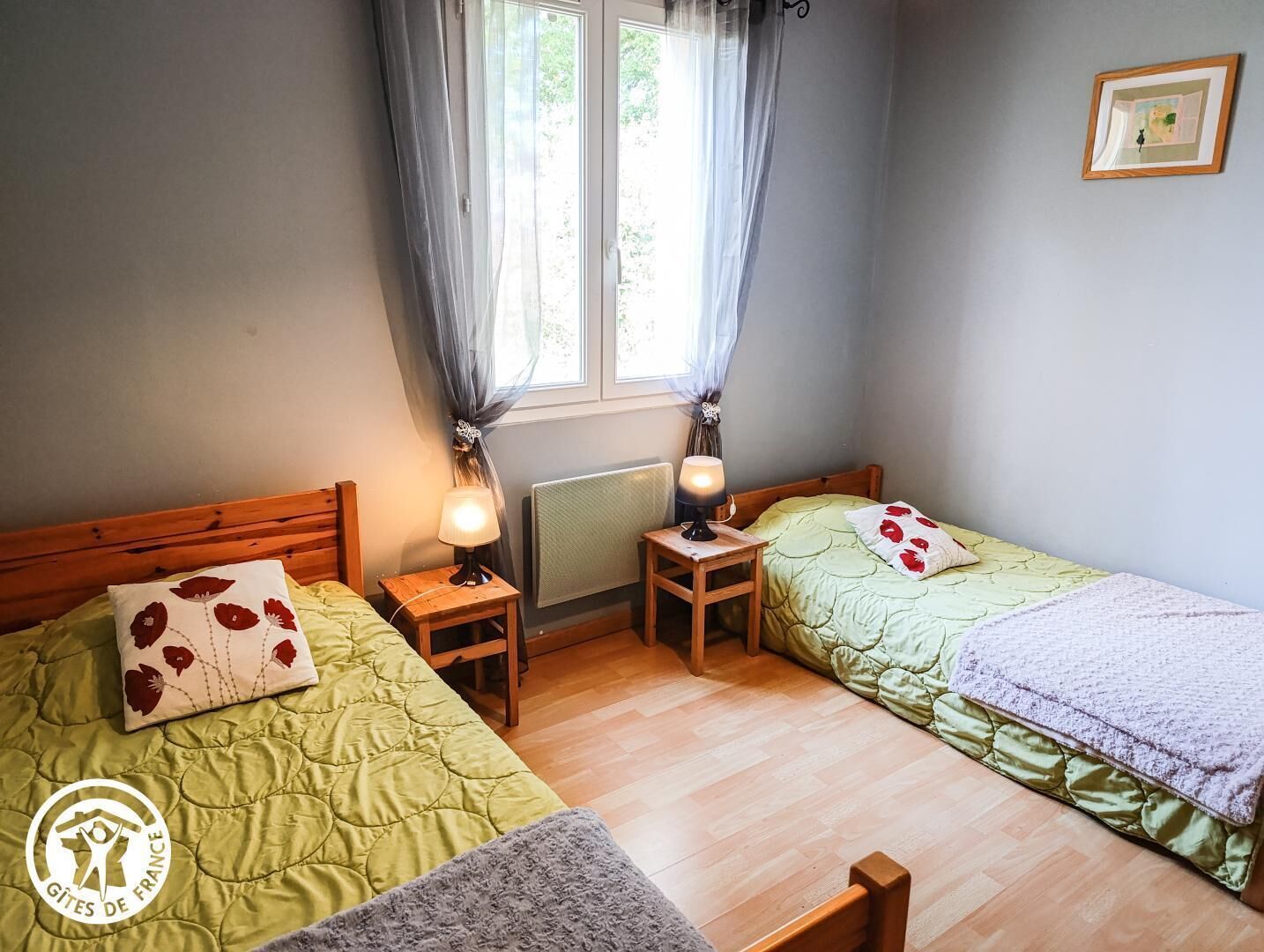 Una habitación con dos camas, una ventana con cortinas, un radiador y una mesita con lámpara.