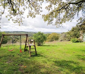 A swing set in a grassy field with a view of distant hills.