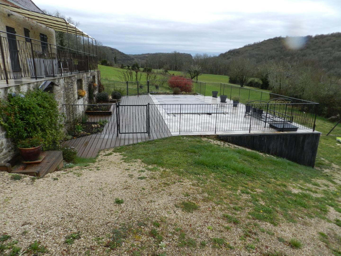 A courtyard with a wooden deck, a black metal fence, and a building with a stone facade.