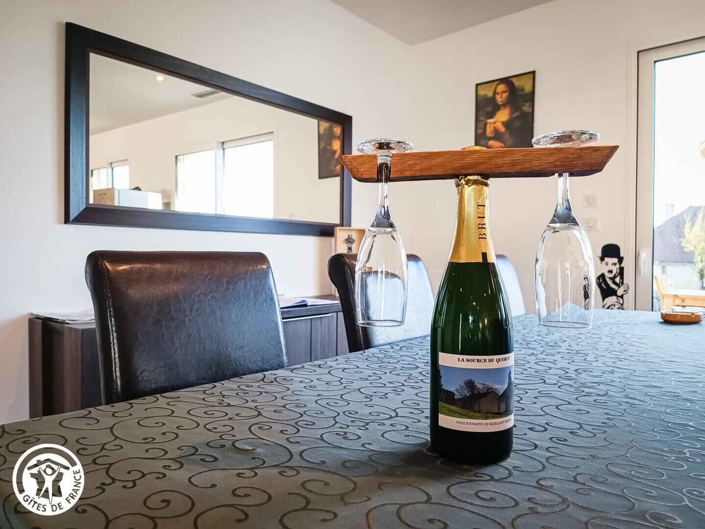 A dining table with a bottle of wine, a wooden wine rack, and a framed picture on the wall.
