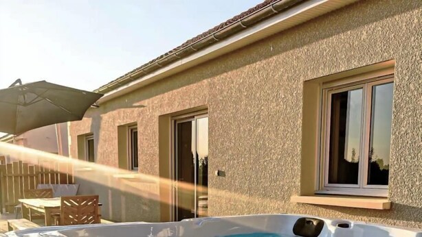 A hot tub in a backyard with a wooden deck and a house in the background. - Gîtes de France® - La Source du Quercy 2 (ALVIGNAC)