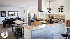 A modern kitchen with a central island, wooden cabinets, and a stainless steel range hood. There are wine bottles on the wall and a vintage toaster on the counter. - Gîtes de France® - La Source du Quercy 2 (ALVIGNAC)