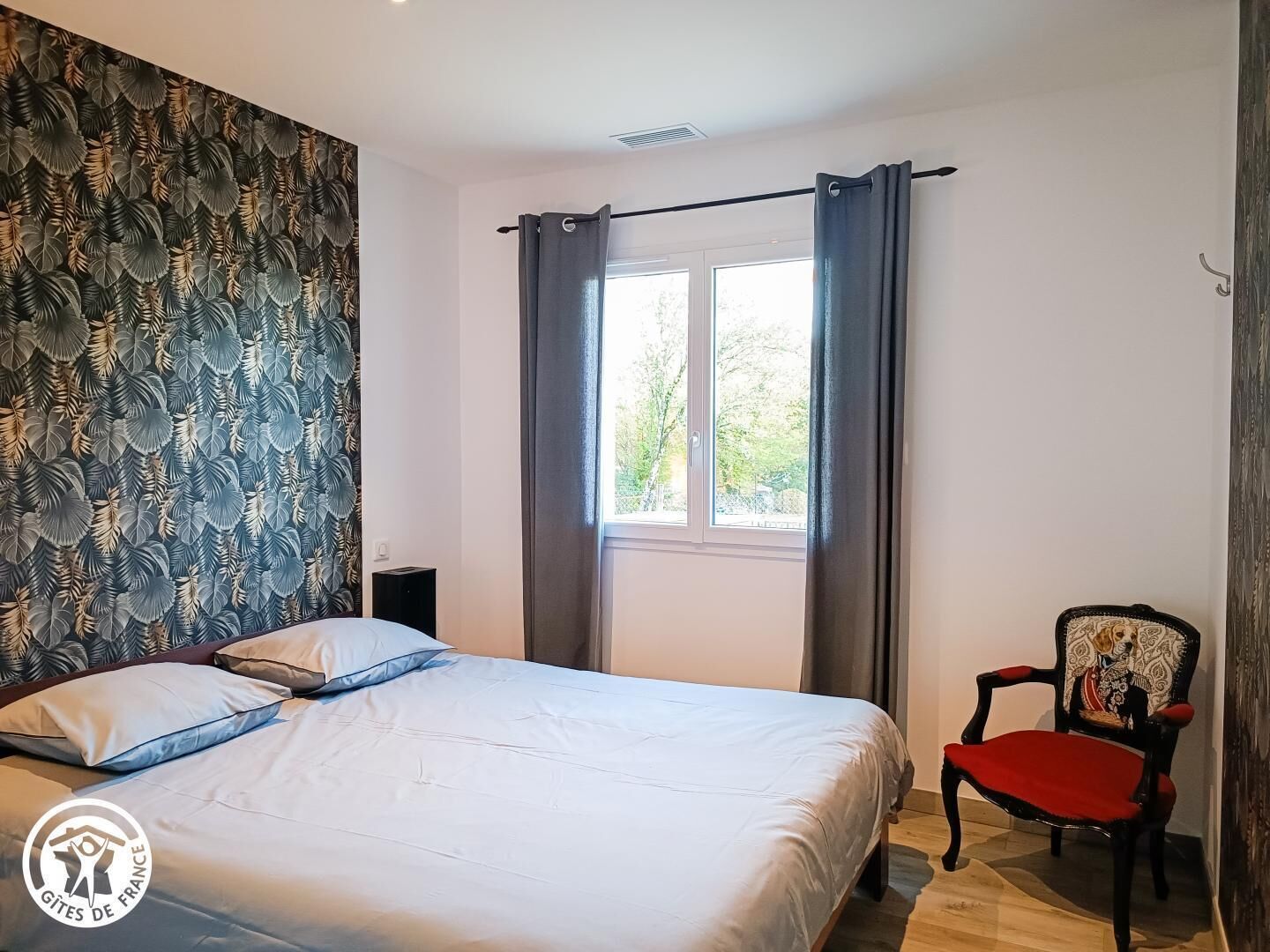 A bedroom with a bed, a chair, a window, and a wall with a leaf pattern.