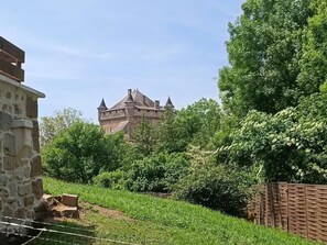A historic stone building with a prominent tower, surrounded by lush greenery and a brick wall.