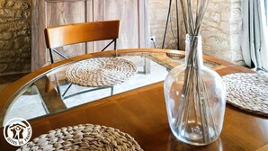 Un coin repas au style rustique, avec une table en bois, un vase en verre contenant des plumes d’herbe des pampas, un mur en pierre et un meuble en bois.