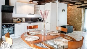 Une cuisine moderne avec des meubles blancs, une cuisinière noire et un coin repas comprenant une table en verre et des sets de table en fibres tressées.