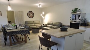 Una cocina moderna con una isla central, comedor con mesa para cuatro, y sala de estar con sofá y sillones.