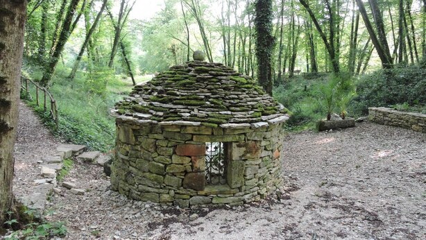 Una estructura de piedra con techo cónico en una zona boscosa.