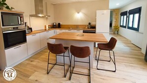 Una cocina moderna con una isla central, dos taburetes de bar, horno empotrado y microondas.