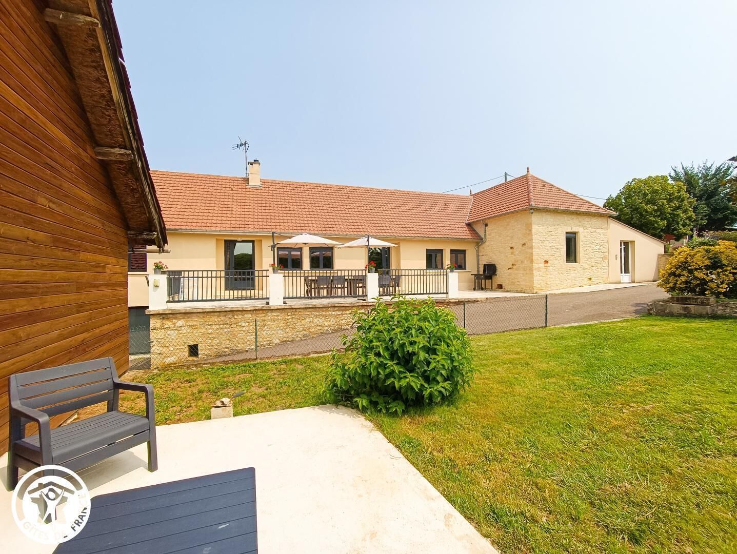 A two-story building with a tiled roof, a covered patio with outdoor seating, and a fenced yard.