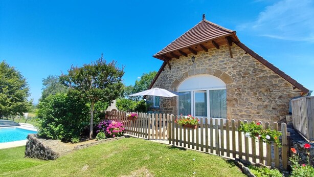A stone house with a wooden fence, a pool, and a garden with flowers.