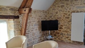 A room with a stone wall, a wooden beam, two white armchairs, a flat-screen TV, and a white radiator.