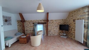 A cozy living room with a stone wall, a wooden ceiling beam, a sofa, a chair, a coffee table, a TV, and a radiator.