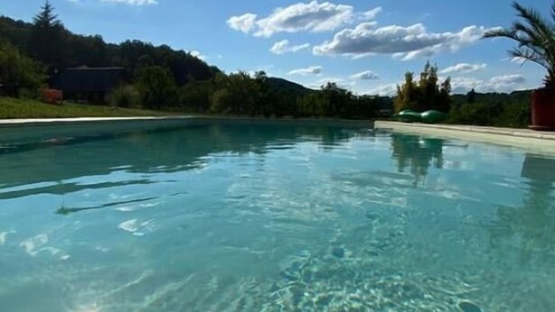 Ein klares Schwimmbecken mit Blick auf einen bewaldeten Hang und ein Gebäude im Hintergrund.