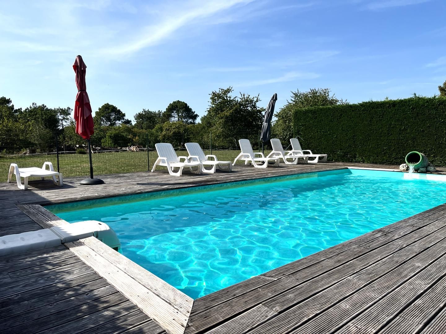 A swimming pool with clear blue water, surrounded by a wooden deck, and white lounge chairs.