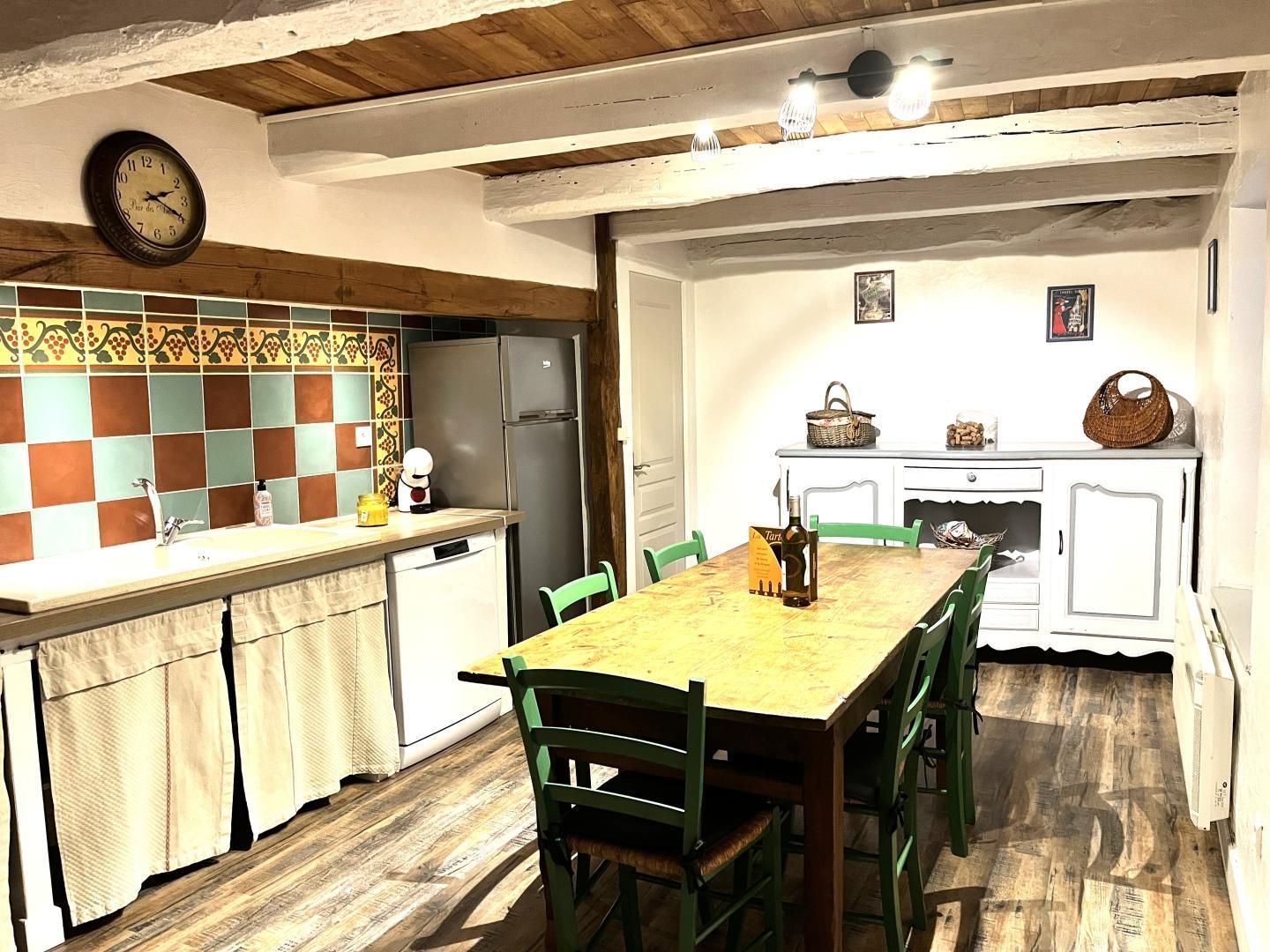A kitchen with a wooden table, green chairs, a refrigerator, and a clock on the wall.