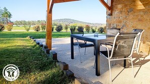 An outdoor patio with a table and chairs, a stone wall, and a view of a grassy field and hills.