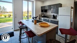 A modern kitchen with a large island, bar stools, and a view of a green landscape.