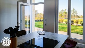 A modern kitchen with a large window, a dining table, and a view of a landscaped garden.