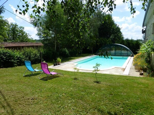 A backyard with a swimming pool, two lounge chairs, and a small garden area.