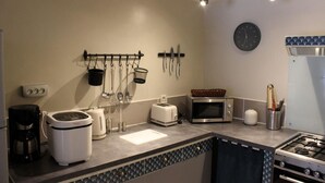 Een moderne keuken met een gasfornuis, een magnetron, een broodrooster en een koffiezetapparaat. Er hangen keukengerei en een klok aan de muur.