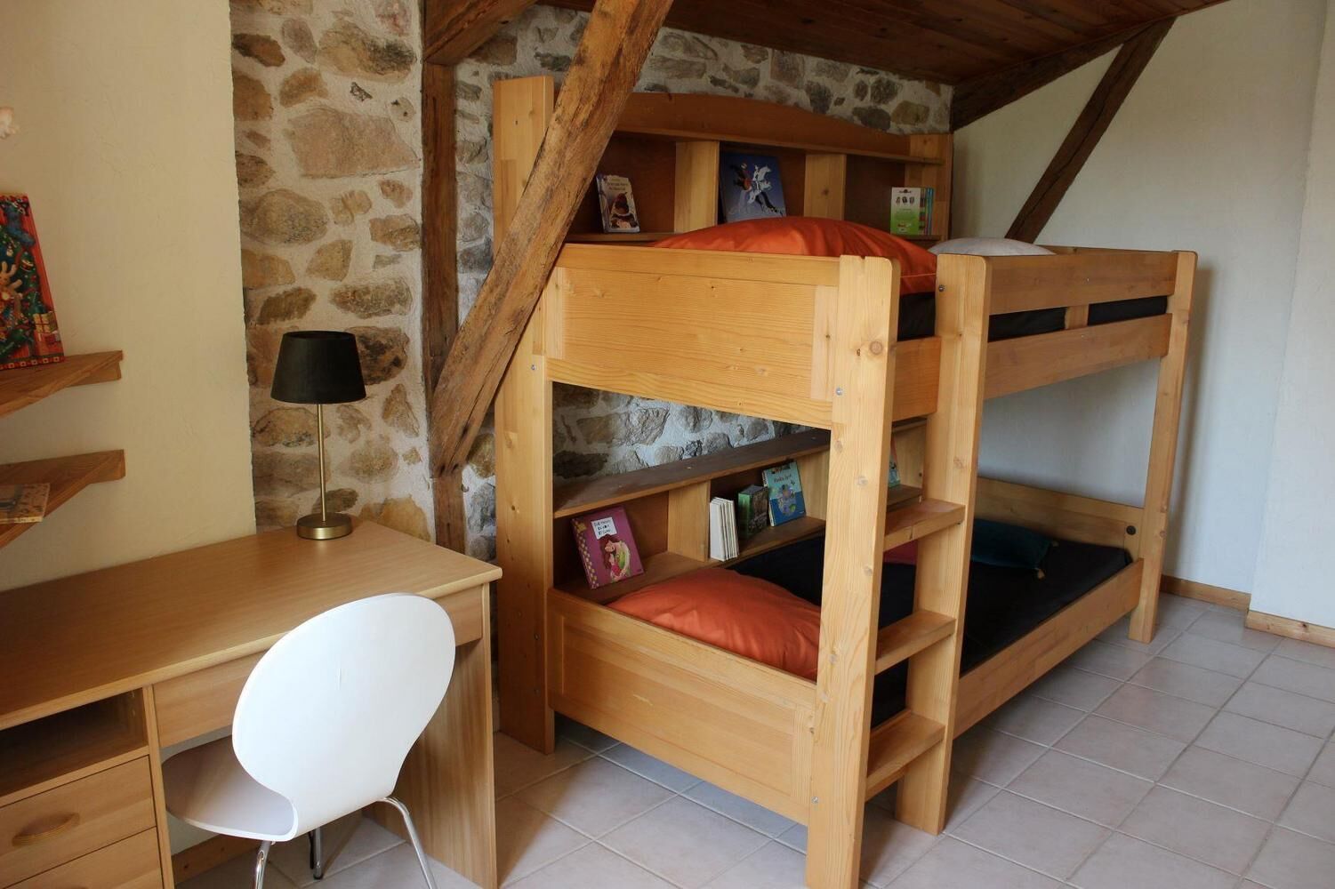 Un lit superposé avec des étagères, un bureau et une chaise, dans une pièce aux murs de pierre et aux poutres en bois.