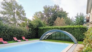 Zwembad met een glazen overkapping, omringd door groen en rode ligbedden.