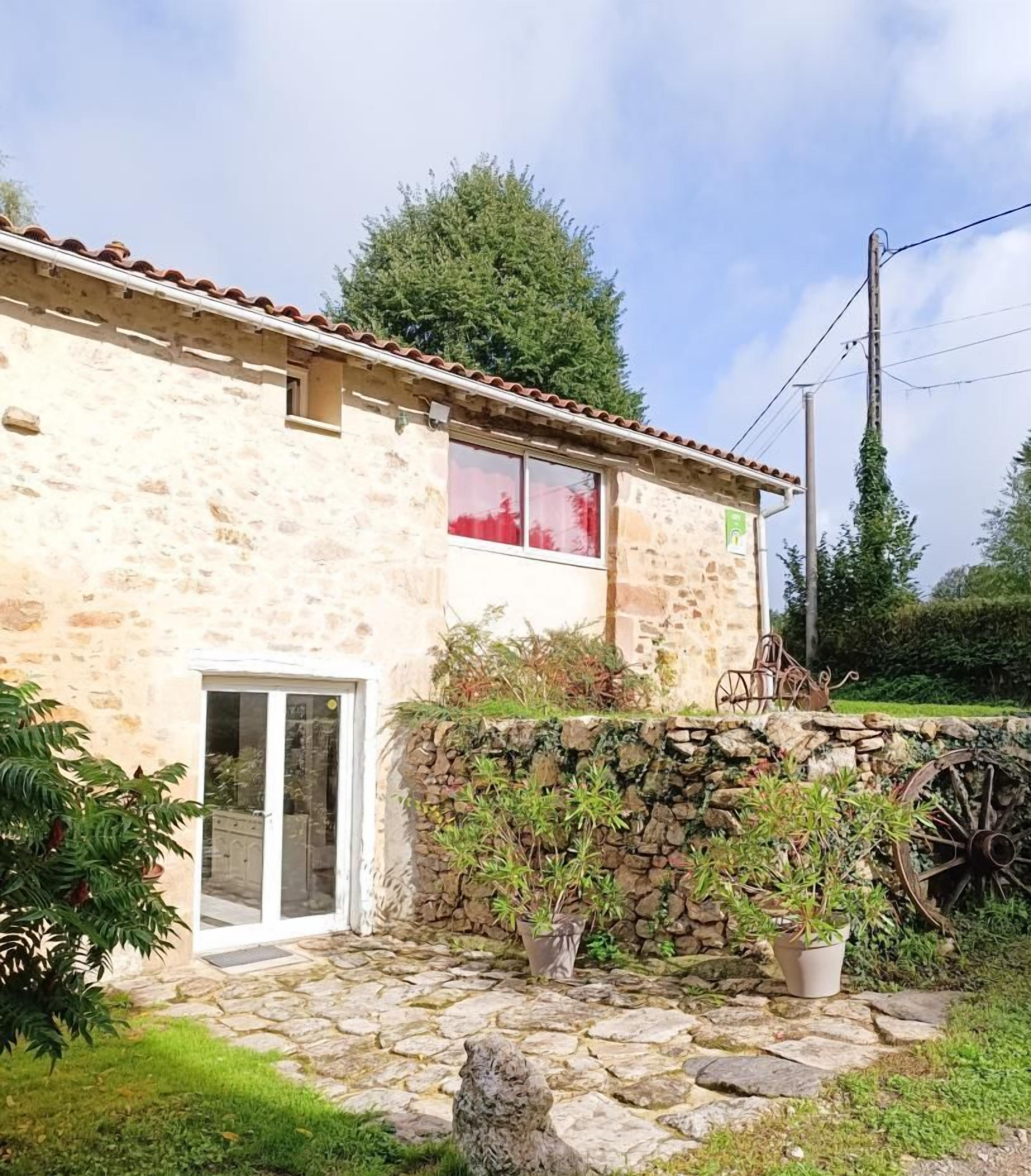 A stone building with a tiled roof, a glass door, and a stone wall with potted plants.