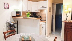 Ett kompakt kök med vita skåp, en mikrovågsugn, en kaffebryggare och ett handfat. Det finns ett matbord med en bordsduk och en krukväxt.