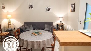 En matplats med ett runt bord, stolar, en soffa och en tv. Det finns konstverk på väggen och en lampa.