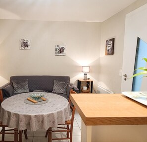 A dining area with a round table, chairs, a sofa, and a TV. There are wall art pieces and a lamp on the wall.
