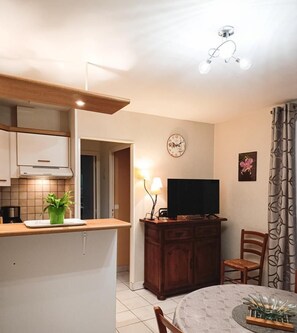 A compact kitchen with a dining area, a clock, and a television.