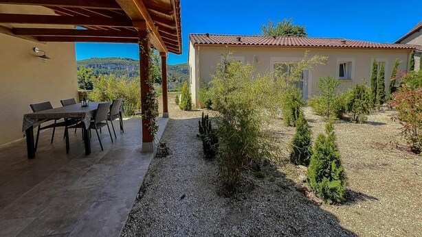 Una veranda riparata con tavolo e sedie, un giardino in ghiaia con arbusti e un edificio con tetto in tegole.