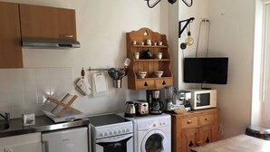 Eine kompakte Küche mit Herd, Backofen, Mikrowelle und Waschmaschine. Ein Holzschrank enthält Geschirr, und an der Wand ist ein Fernseher befestigt.