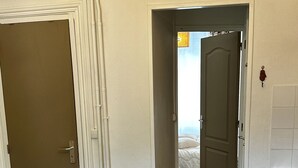 Ein Zimmer mit Holzboden, einem dunklen Teppich, einer weißen Tür und einem Flur, der zum Schlafzimmer mit einem Bett führt.