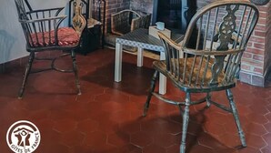Un intérieur rustique avec une cheminée en briques, des poutres en bois et des chaises d’époque.