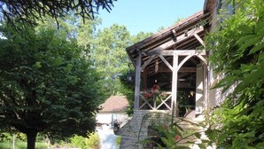 A stone pathway leading to a wooden porch with a stone wall and a hanging flower basket. - Gîtes de France® - Le Mazet (SAINT-MEDARD)