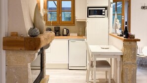 A compact kitchen with white cabinets, a microwave, and a stone countertop. - Gîtes de France® - Le Mazet (SAINT-MEDARD)