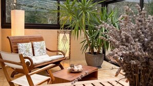 A wooden outdoor seating area with a cushioned chair, a small table, and a potted plant. - Gîtes de France® - Le Mazet (SAINT-MEDARD)