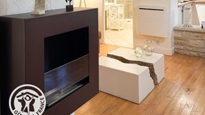 Een moderne woonkamer met een open haard, een witte salontafel en een zichtbare keuken door een open deur.