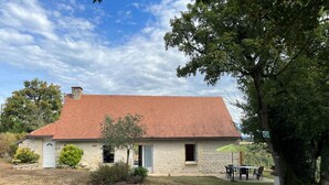 Ein Haus aus Stein mit rotem Dach, einem kleinen Garten und einem Tisch mit Stühlen davor.