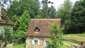 Ein Haus aus Stein mit Ziegeldach, umgeben von Grün und einem gepflegten Rasen.