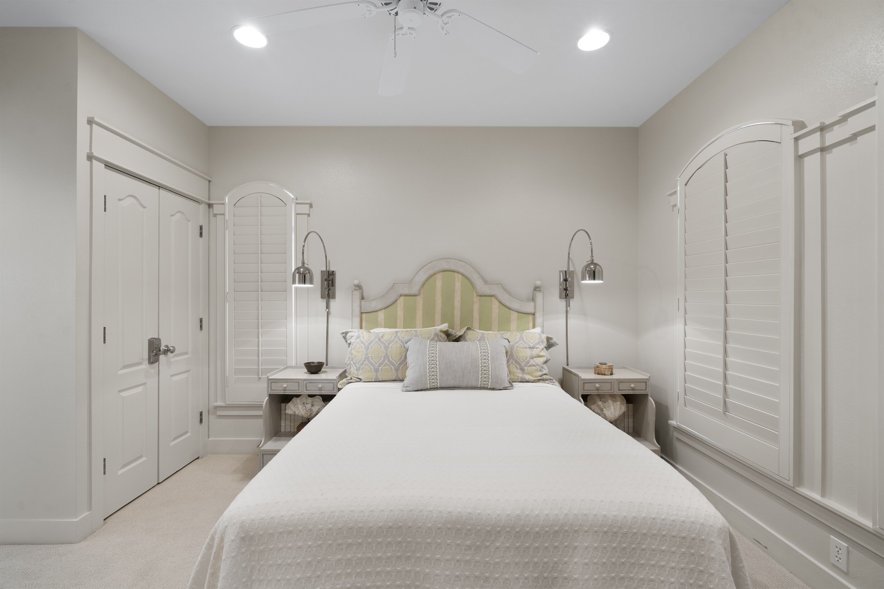 A bedroom with a large bed, two nightstands, a ceiling fan, and a wardrobe.