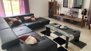 Uma sala de estar moderna com um sofá de couro preto, uma mesa de centro de vidro e um móvel de entretenimento de madeira com uma televisão de tela plana.