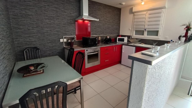 Uma cozinha moderna com armários vermelhos, uma ilha central e uma área de refeições com cadeiras.