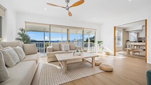 Een ruime woonkamer met balkon, plafondventilator en uitzicht op de lucht.