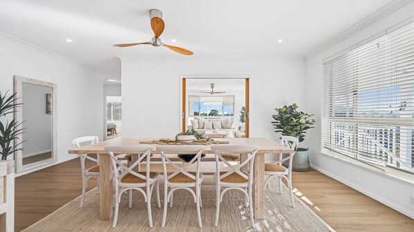 A modern dining area with a wooden table, white chairs, and a ceiling fan.