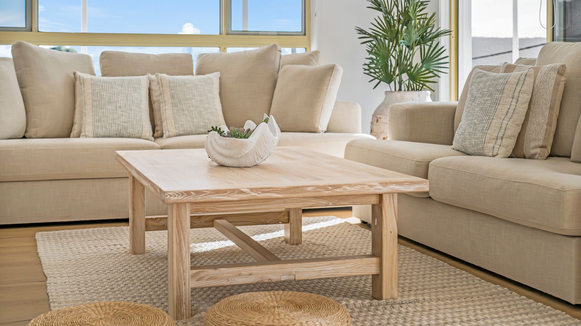 A living room with a beige sofa, a wooden coffee table, and a woven rug.