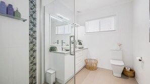 Een moderne badkamer met een douchecabine van glas, een wit wastafelmeubel met een waskom en een toilet.